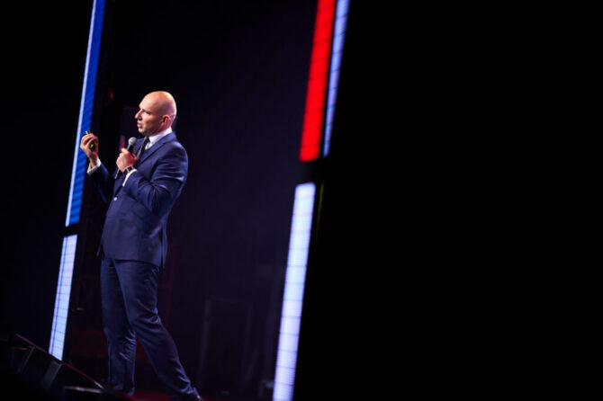 Speaker na pódiu počas firemnej konferencie, zachytený v dynamickom svetle a reálnej eventovej atmosfére.